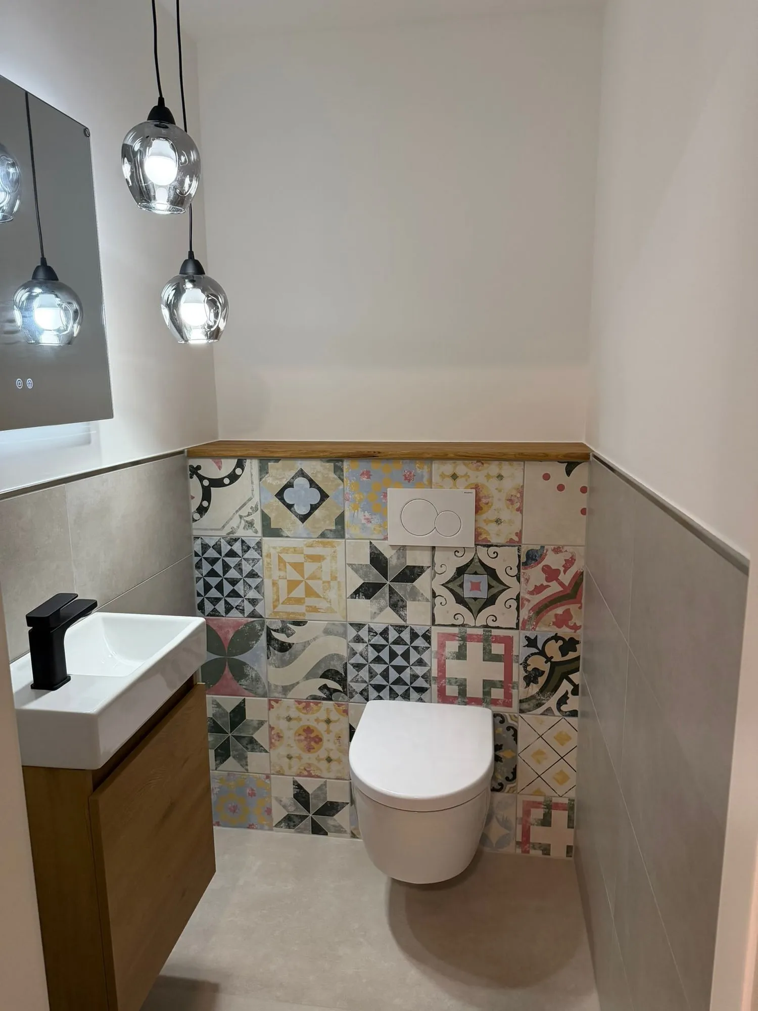 Gäste-WC mit bunten Zementfliesen hinter dem Wand-WC und hellem Boden