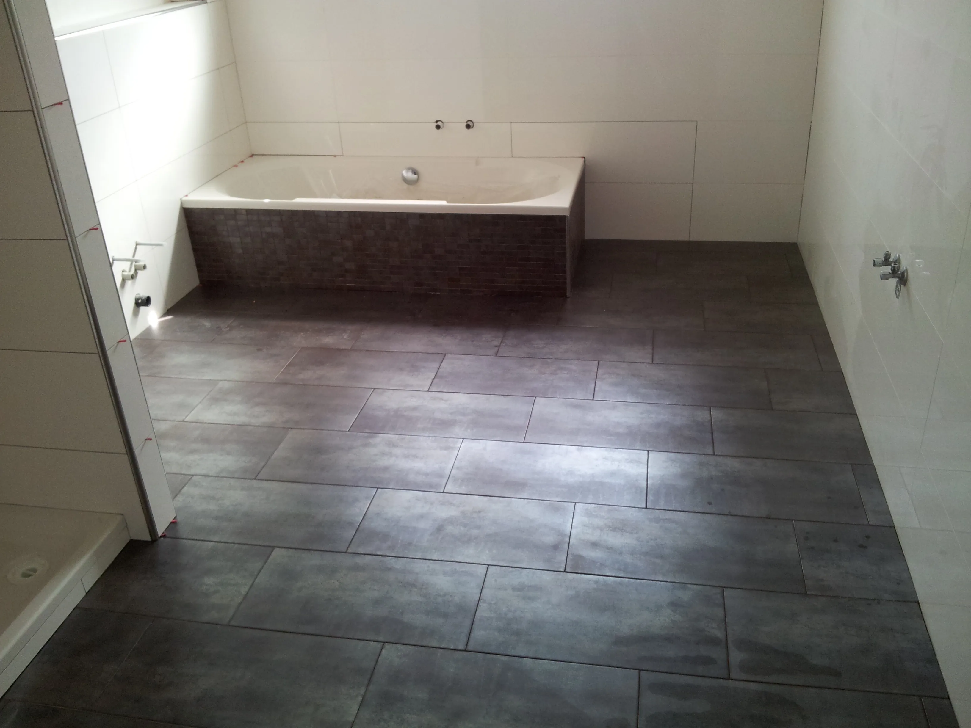 Badezimmer mit großformatigen Wandfliesen und Mosaikstreifen in Duschnähe