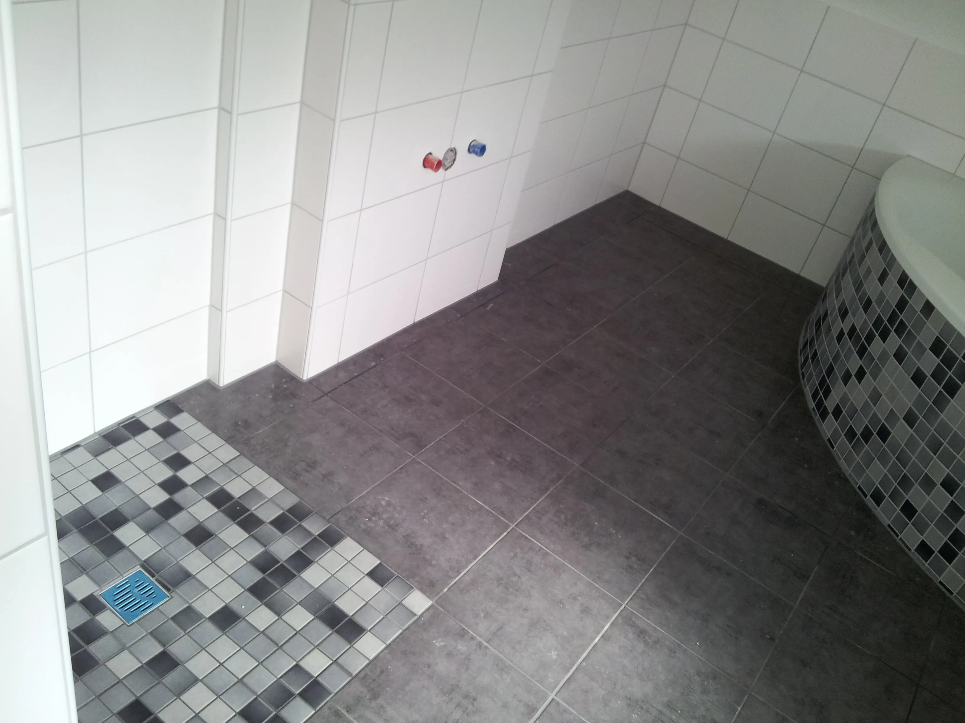 Bad mit dunklem Fliesenboden, Duschfläche aus grauem Mosaik und mosaikverkleideter Eckwanne