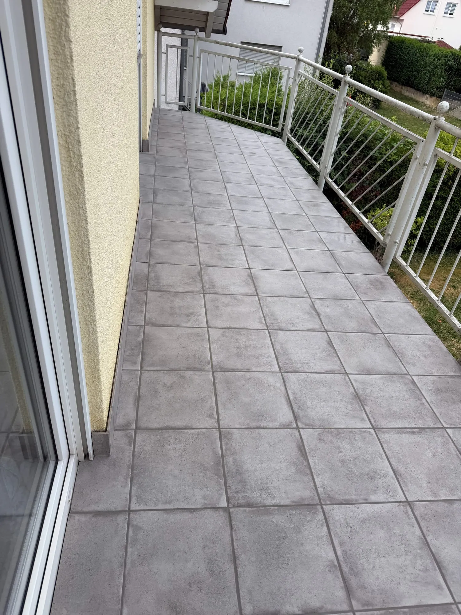 Langer, schmaler Balkon mit grauen Platten entlang der Hauswand und Metallgeländer
