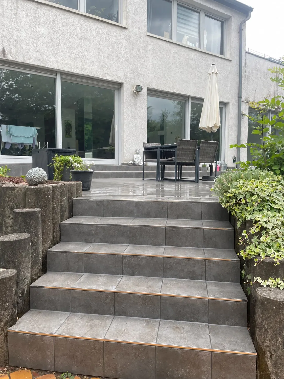 Breite Außentreppe mit grauen Platten, die vom Garten zur Terrasse hinaufführt