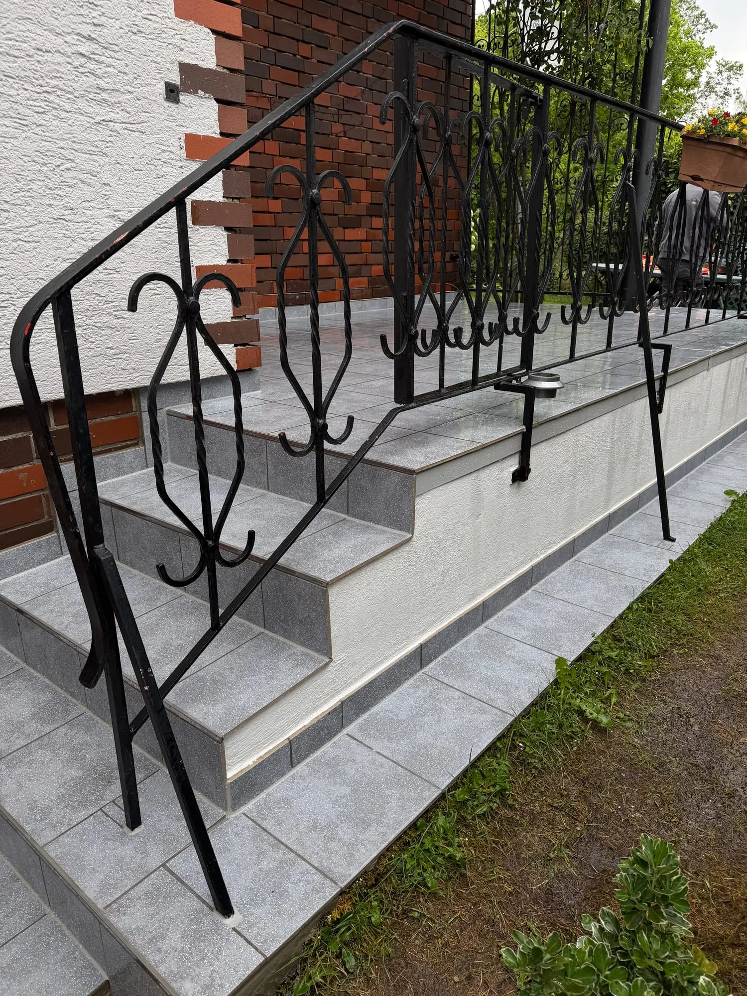 Treppe zur Terrasse mit grauen Plattenstufen und verziertem Schmiedegeländer