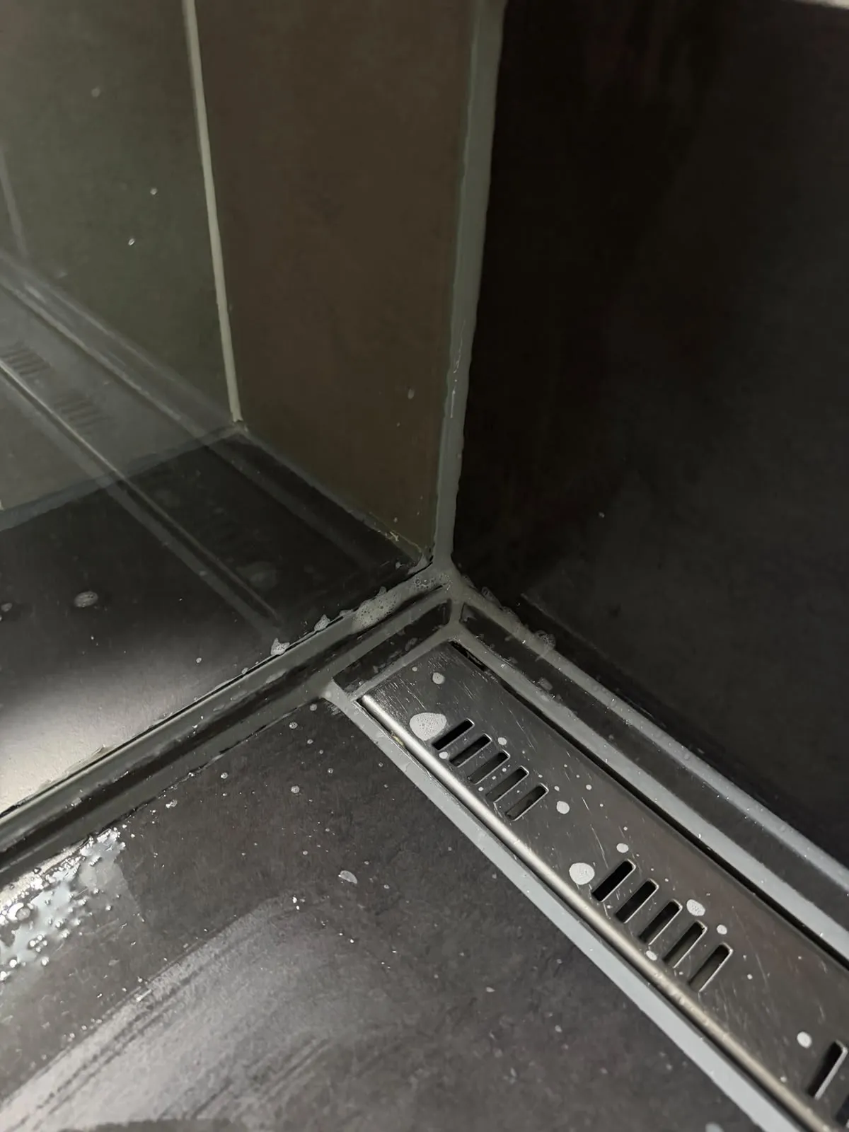 Dieselbe Duschecke nach der Erneuerung mit frischen, sauber gezogenen Silikonfugen an Glaswand, Wand und Rinne